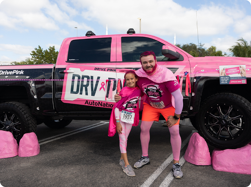 A father and daughter dressed up as superheroes standing in front of the side of an autonation truck